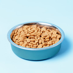 A bowl of dry food in the iron bowl on blue background