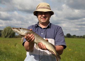 The fisherman holds a big pike in his hands, an excellent catch. Fishing on the Dnieper River in summer.
