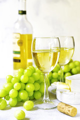Two glasses of white wine,cheese and grapes .