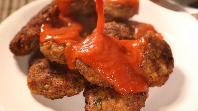 Pouring tomato sauce on fresh meatballs on plate