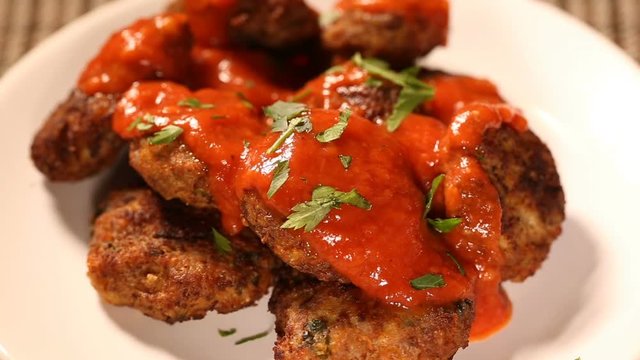 Spreading fresh parsley on meatballs with tomato sauce on plate