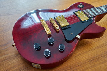 Shiny Wine Red Guitar With Golden Hardware Placed On A Wooden Table Angled Side View Focus On Stop Bar And Pickups