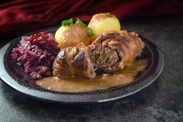 beef roulades, traditional german meal, filled meat rolls with red cabbage, potatoes and sauce on a dark plate and slate stone