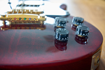 Tone And Volume Knobs On a Shiny Wine Red Guitar With Golden Hardware Placed On A Wooden Table 