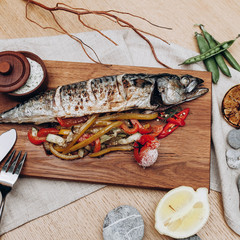 beautifully served table with baked mackerel with vegetables on a wooden board with white sauce and half a lemon