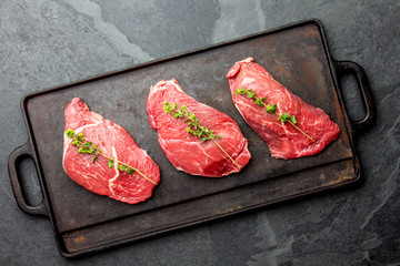 Raw beef steaks with herbs and spices on cast iron frying board, top view