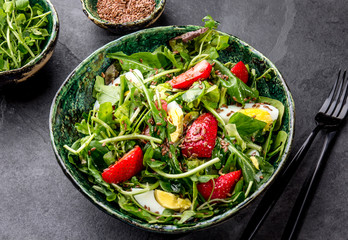 Green leaves and srawberry salad with linen seeds in green bowl, gray background