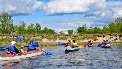 Group of tourists kayaking on the river with green trees, bright blue sky with clouds at beautiful...