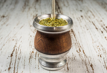 Traditional Argentinian yerba mate tea in a calabash gourd with bombilla stick against wooden background