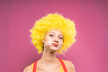 funny girl in bright yellow wig with chupa chups smiles into the camera