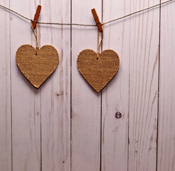 Two brown hearts hanging on a line in front of a white wooden fence