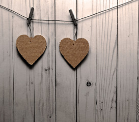Two brown hearts hanging on a line in front of a white wooden fence