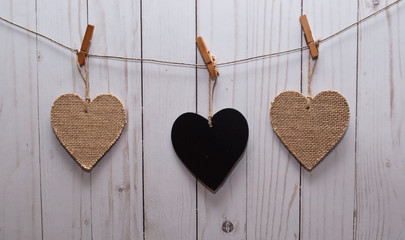 Three hearts, one black and two brown hanging on a line in front of a white wooden fence
