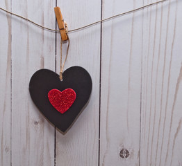A single black heart with a smaller red heart in it's center hanging on a line in front of a white wooden fence