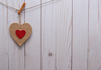 A single brown heart with a smaller red heart in it;s center hanging on a line in front of a white wooden fence