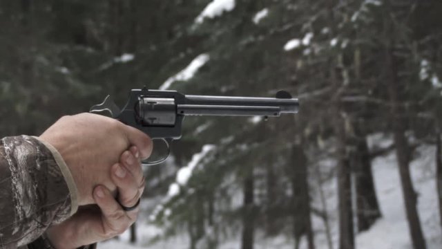 Man in hunting clothing aims and shoots his revolver gun, various framing from medium to close up shot, with sound.