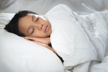 Obraz na płótnie Canvas boy sleeping on bed with white sheet and pillow.asian kid fall asleep daydreaming.sleep concept