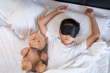 boy sleeping on bed with teddy bear white pillow and sheets wearing sleep mask.boy fall asleep in morning.sleep concept