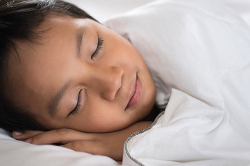 Fototapeta na wymiar boy sleeping with smile face on white bed sheet and pillow.boy fall asleep with smiling face having sweet dream.sleep concept