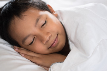 Obraz na płótnie Canvas boy sleeping with smile face on white bed sheet and pillow.boy fall asleep with smiling face having sweet dream.sleep concept