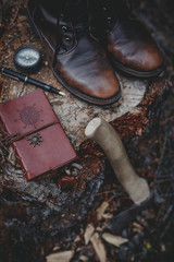 Travel tourist set is boots, compas, pen, notepad and axe on wood