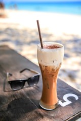 Shallow depth of field of ice coffee on wood table and sunglasses at the beach.