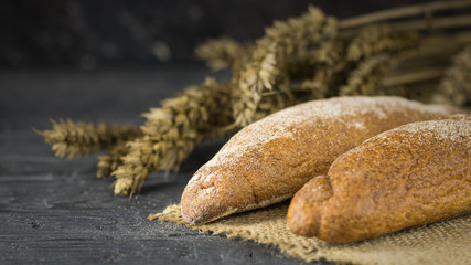 Two freshly made baguette from wheat flour on a piece of burlap with ears on the table.