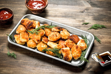 Chicken nuggets on a steel tray with sauce.
