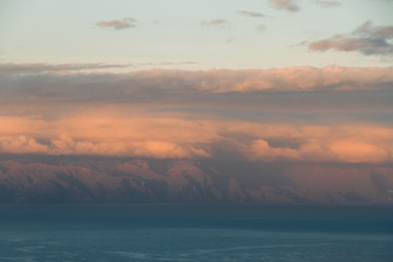 Sunset light behind clouds above mountains and ocean