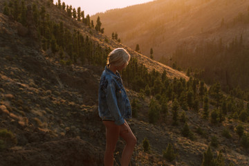 Girl in mini shorts and jeans jacket hiking and looking at sunset in desert nature