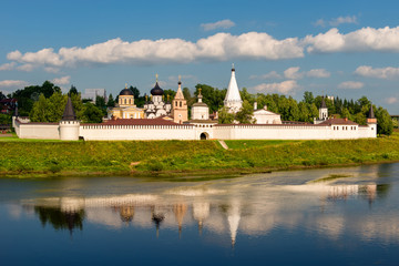 Fototapeta na wymiar View on ancient white-stone Convent of the Dormition built in 16 century on Volga River bank with reflection in water. Staritsa, Tverskoy region, Russia.