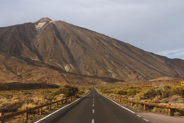 Long straight road in mountains with volcano in background
