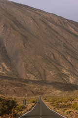 Obraz premium Long straight road in mountains with volcano in background