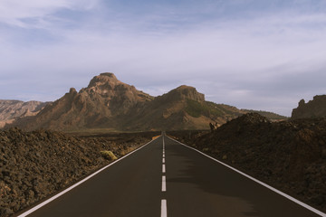 Long straight road in mountains with volcano in background