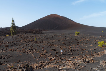 Girl walking in dark volcanic landscape with green trees