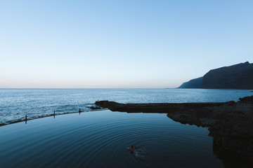 Man swimming in calm water in natural pool near ocean at dawn