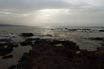 Fototapeta na wymiar Ladder to ocean on rocky beach in cloudy weather