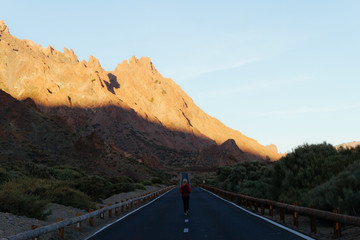 Woman walking on road with sunrise light on volcanic hills in desert landscape