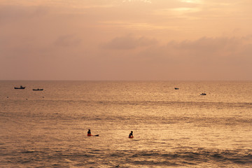 Surfers in ocean waiting for waves while sunset