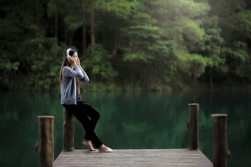 Beautiful young woman with headphones relaxing on the dock