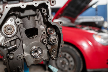Fototapeta na wymiar Selective focus. Engine Block on a repair stand with Piston and Connecting Rod of Automotive technology. Blurred red car on background. Interior of a car repair shop.