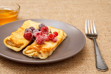 Homemade pancakes filled with cottage cheese and topped with frozen raspberries and blackberries on plate, honey in bowl