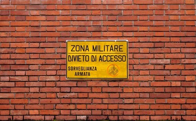 Military area, no access, armed surveillance. Warning sign in italian language on brick wall background