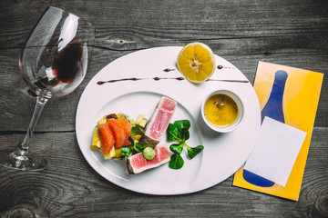 Tuna steak with sauce tartar grapefruit, lemon, peach, spinach, dried tomatoes and a glass of red wine. Wooden gray background and space for writing