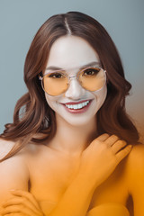 Fototapeta premium cheerful girl posing in yellow sunglasses, isolated on grey