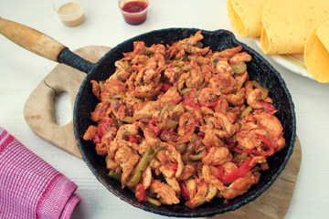 Chicken stew with red and green pepper, with red onion, pickled cucumber and spices in a frying pan.