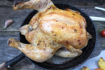 Appetizing baked chicken is located in an old frying pan on a wooden background.