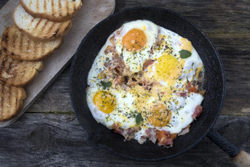 Fried eggs in an old frying pan and fried bread on a wooden background.