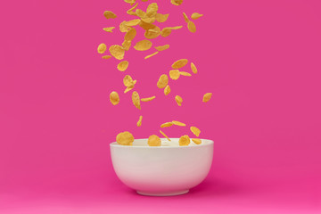 close-up view of delicious corn flakes falling into white bowl isolated on pink