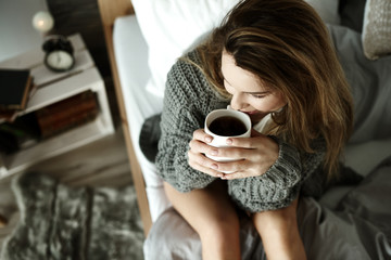 Attractive woman drinking coffee in bed .
